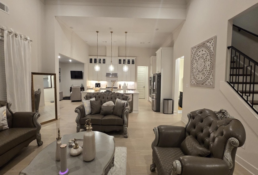 Spacious open-concept living area featuring high vaulted ceilings, light wood-finish flooring, and a contemporary kitchen with white cabinetry and an island with pendant lighting