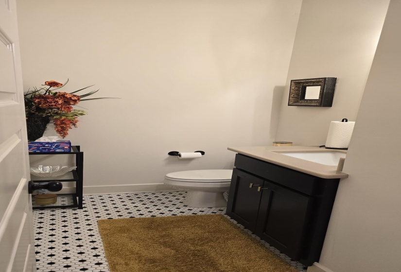 Powder room featuring black and white hexagonal tile flooring, a dark wood vanity with a light-colored countertop and integrated sink, a white toilet, and neutral wall paint