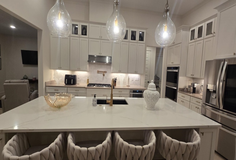 Kitchen featuring a large central island with seating, pendant lighting, stainless steel double ovens, a gas range with a stainless steel vent hood, and white cabinetry
