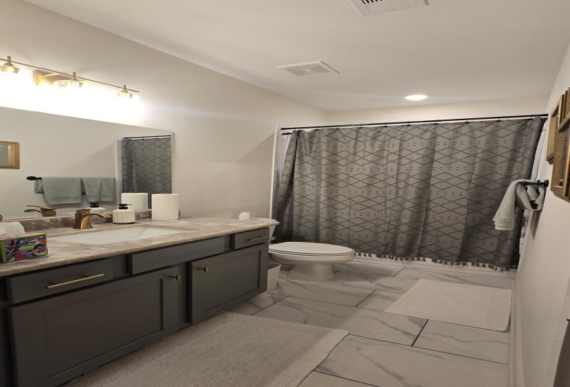 Contemporary bathroom featuring a vanity with dark gray cabinetry and gold-tone hardware, a light-colored countertop with an integrated sink, and a modern gold-tone faucet