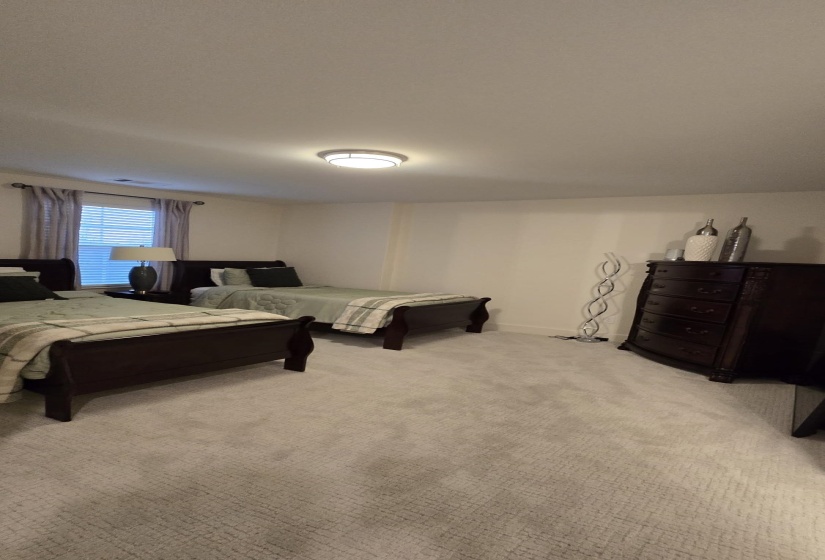 Plush gray carpeting extends throughout this room, featuring a window with horizontal blinds and drapery, white baseboards, and a flush-mount ceiling light