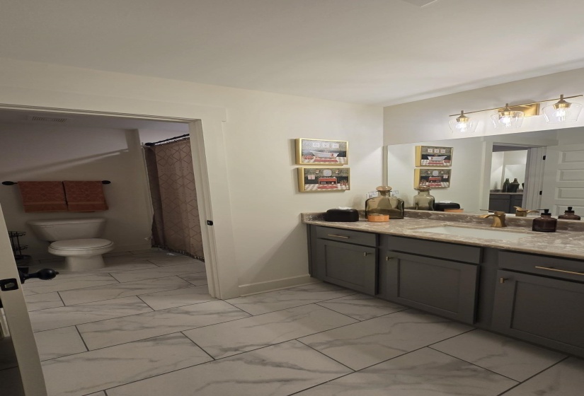 Bathroom vanity featuring a light-colored countertop, dual sinks with gold-finish faucets, and dark gray cabinetry with gold-finish hardware