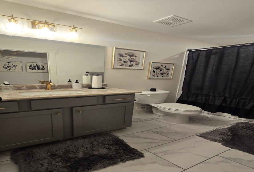 Bathroom featuring a vanity with dark gray cabinetry, gold-finish hardware, and a light-toned countertop with an integrated sink