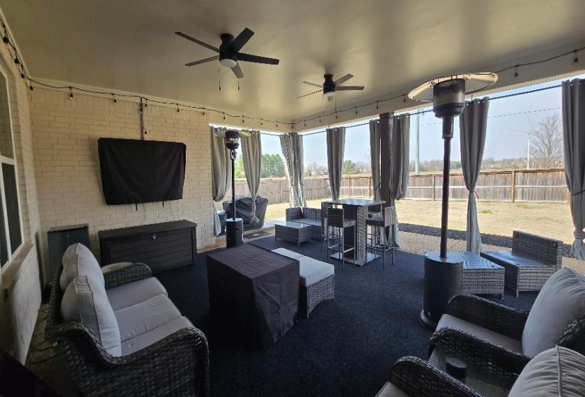 Expansive covered patio featuring a white brick exterior wall, dual ceiling fans, string lighting, and a fenced backyard