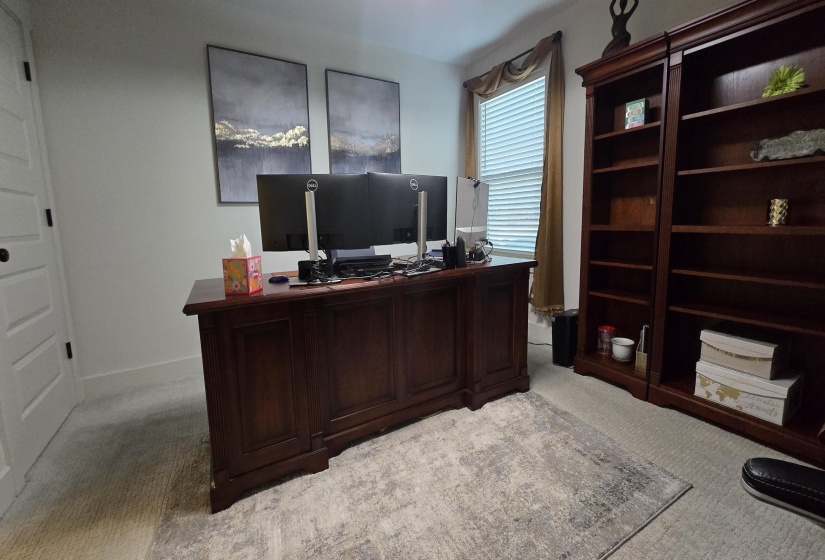 Dedicated workspace featuring a built-in executive desk with rich wood-finish, coordinating full-height bookshelves, a window with blinds and valance, and neutral wall paint