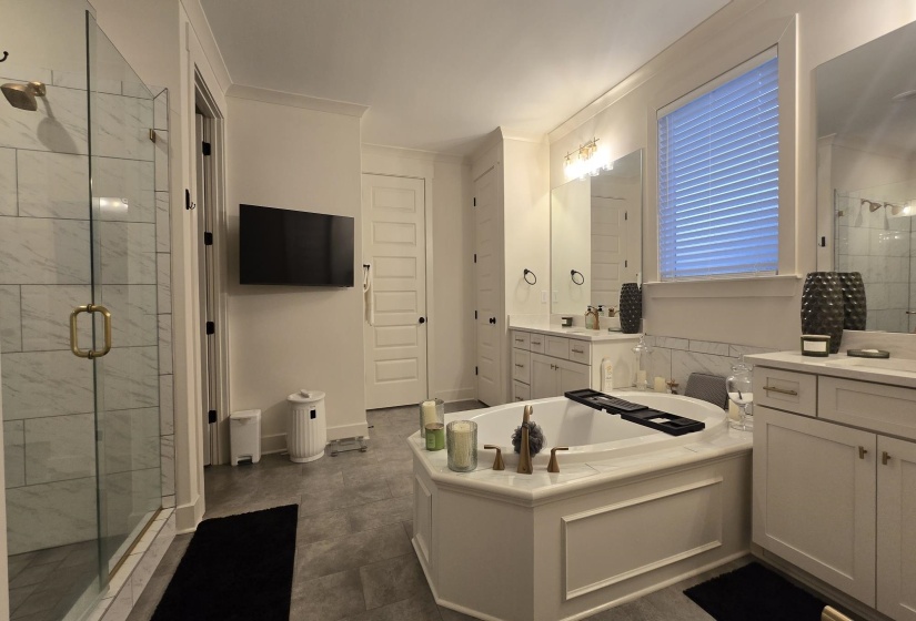 Spacious bathroom featuring an oval-shaped soaking tub, dual vanity with undermount sinks, separate glass-enclosed shower, and tile flooring