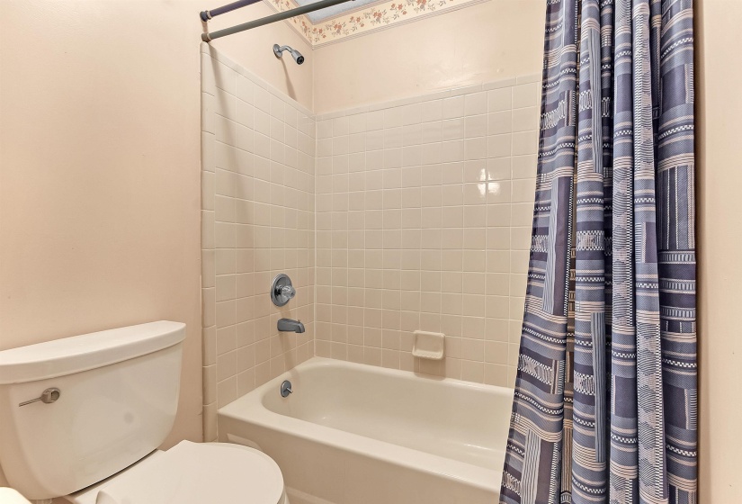 Bathroom featuring a built-in bathtub with ceramic tile surround, chrome fixtures, and a white toilet