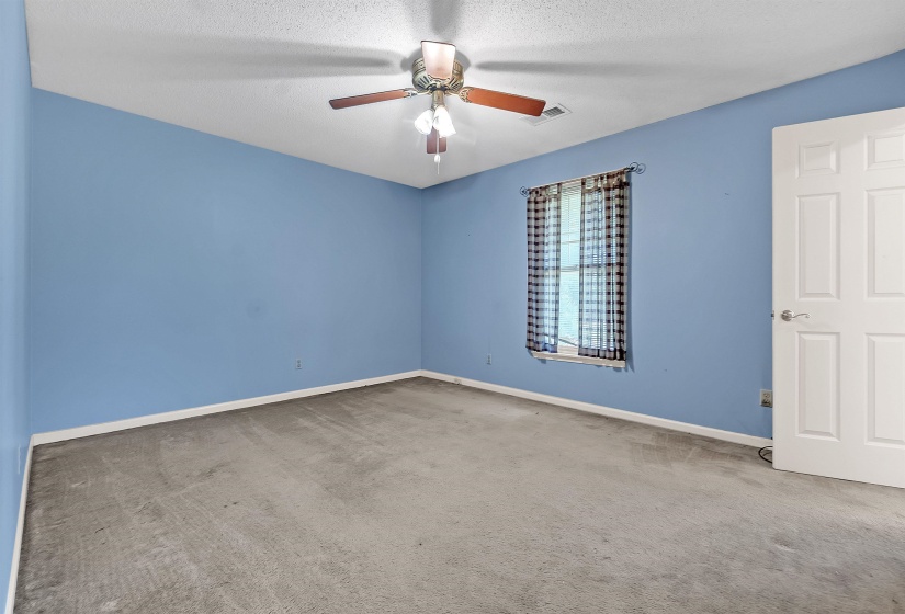 Spacious room featuring a ceiling fan with light fixture, single window with patterned curtains, and a white paneled door