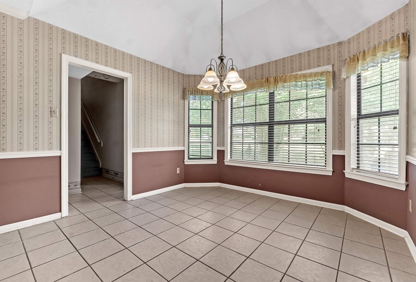 Dining area featuring ceramic tile flooring, three large windows with horizontal blinds, a vaulted ceiling, and a multi-bulb chandelier