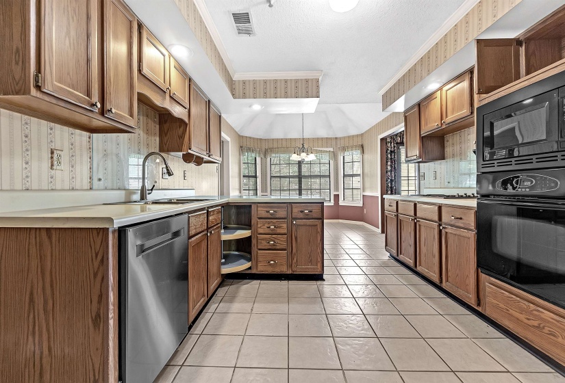 Kitchen featuring wood cabinetry, integrated stainless steel dishwasher, double basin sink with gooseneck faucet, light-toned countertops, and tile flooring