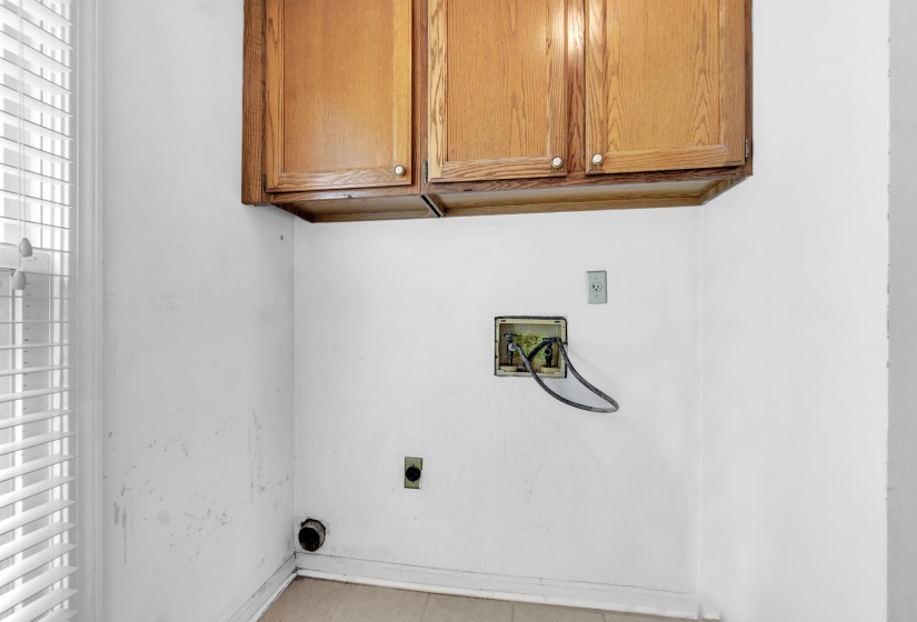 Dedicated utility space featuring overhead wood cabinetry and a window with horizontal blinds