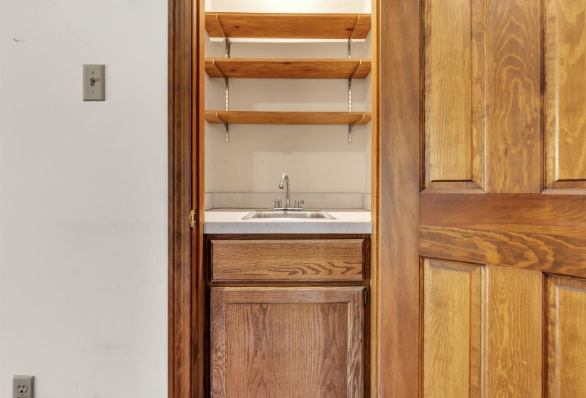 Compact wet bar featuring a stainless steel sink with a single-handle faucet, light-toned countertop, and wood-finish cabinetry