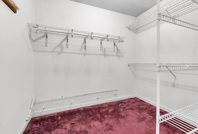 Spacious closet with white wire shelving, a textured white ceiling, and burgundy carpet flooring