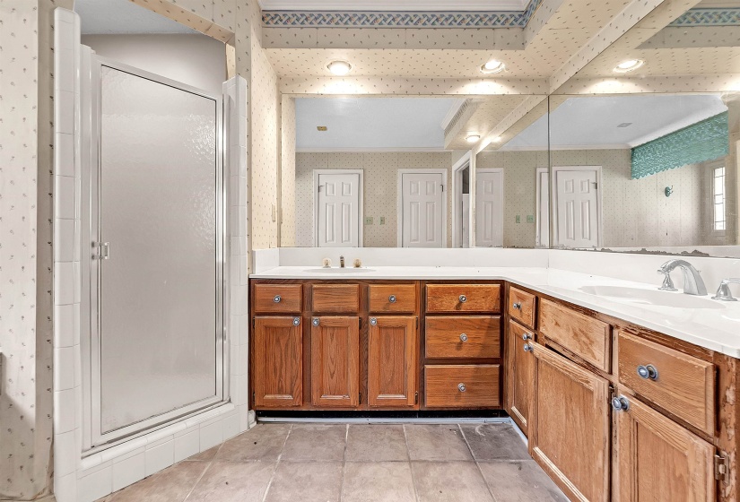 Bathroom featuring a wood-finish vanity with dual sinks, a large wall-mounted mirror, and a standing shower with a frosted glass door