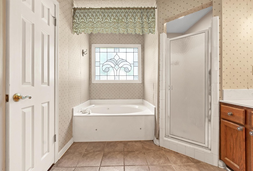 Bathroom featuring a jetted tub, a decorative stained glass window, and a stand-alone shower with a frosted glass door