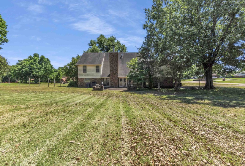 Expansive grassy area with mature trees and a two-story residence featuring a prominent stone chimney