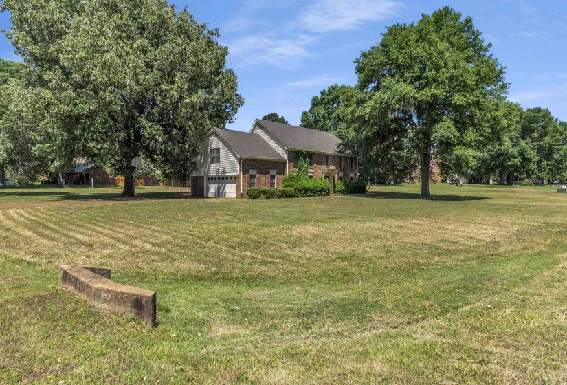 Expansive front lawn with mature trees and a brick and siding exterior