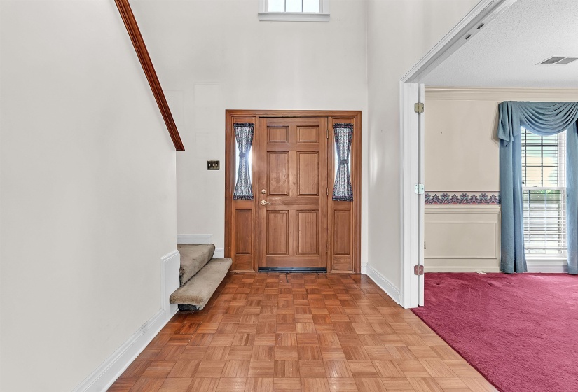 Entryway featuring wood-finish parquet flooring, a paneled solid wood front door with sidelights, and a high ceiling