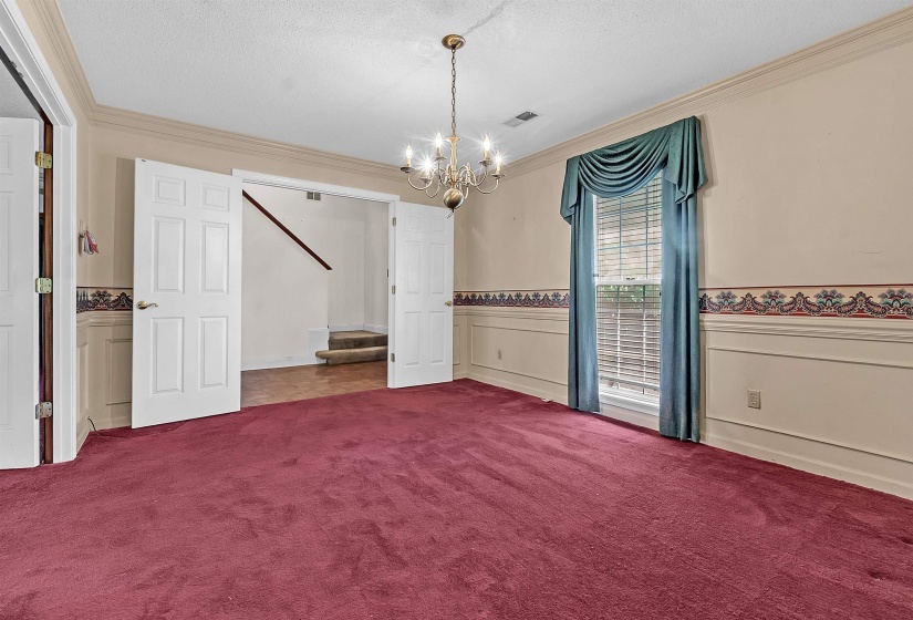 Spacious room featuring broadloom carpeting, a multi-pane window with blinds, and white wainscoting