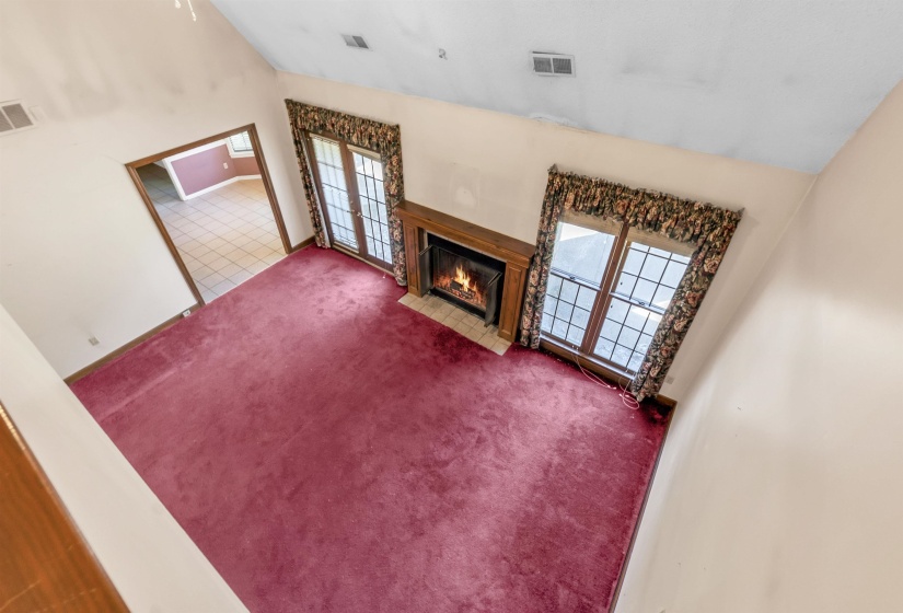 Living room with a vaulted ceiling, a wood-finish mantel fireplace, and two sets of double-pane windows