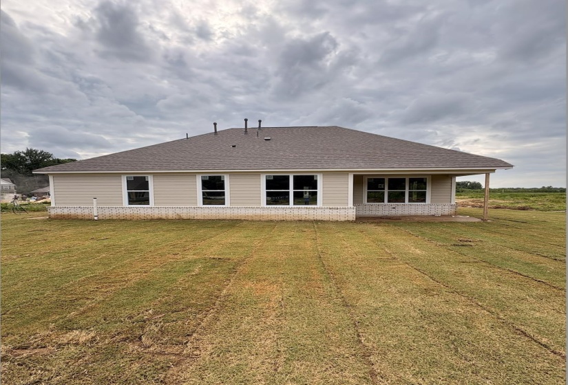 Rear exterior featuring beige horizontal siding, white brick foundation, a brown shingle roof, and multiple white-framed windows