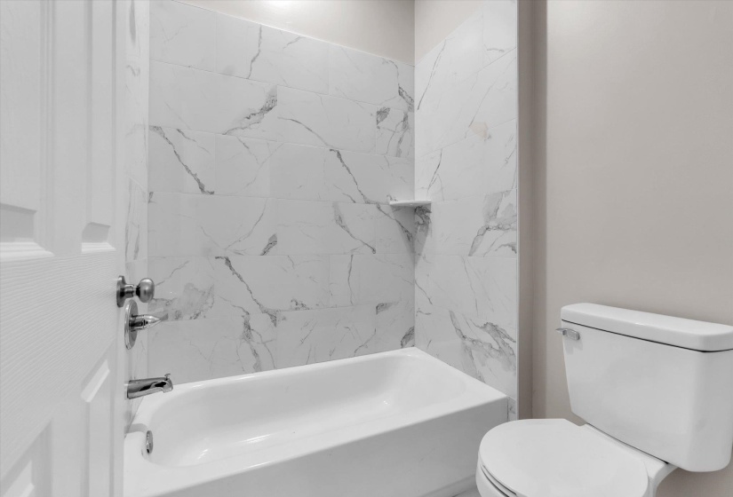 Bathtub and shower combination featuring white marble-look subway tile surround with a built-in niche