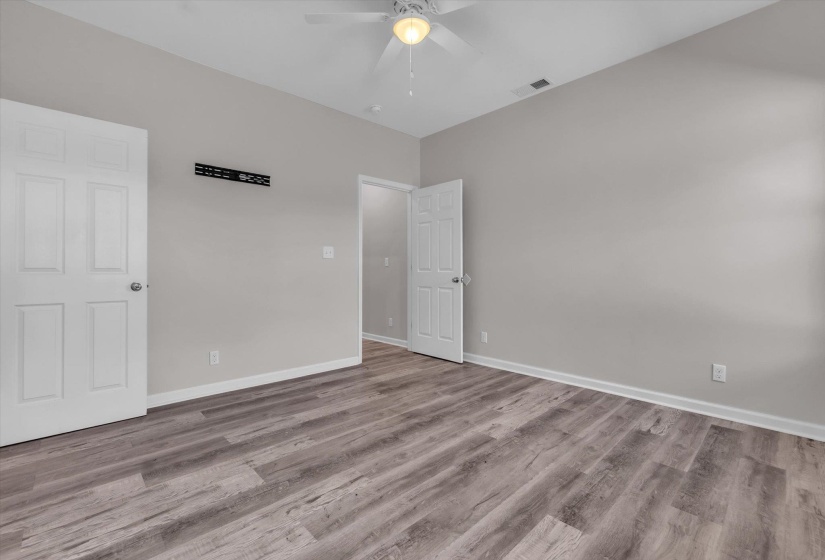 Spacious room featuring wood-finish flooring, light gray walls, white baseboards, and a ceiling fan with integrated lighting
