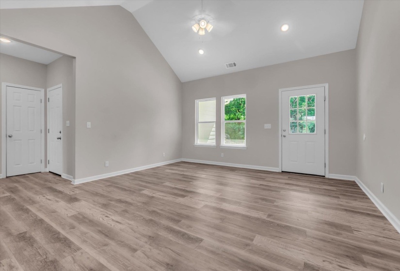 Spacious room featuring vaulted ceilings, wood-finish flooring, recessed lighting, and a multi-pane glass door