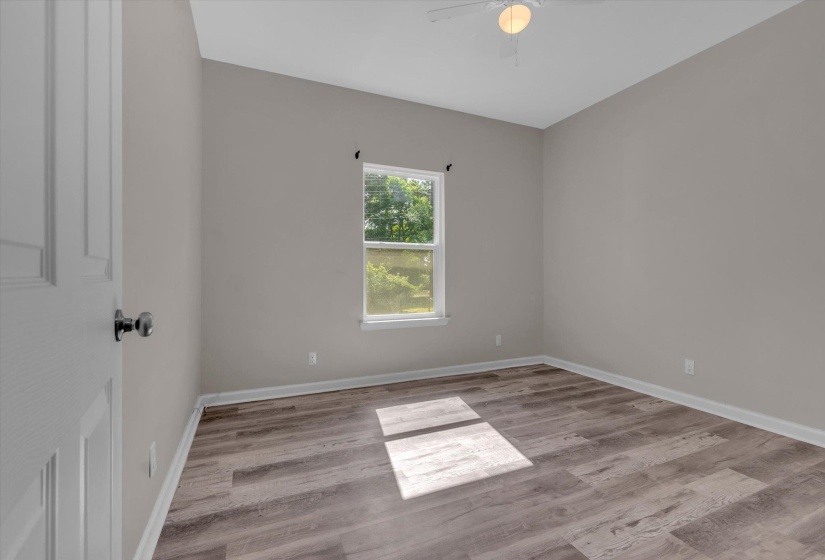 Spacious room featuring wood-finish flooring, a ceiling fan, and a paneled door with dark hardware