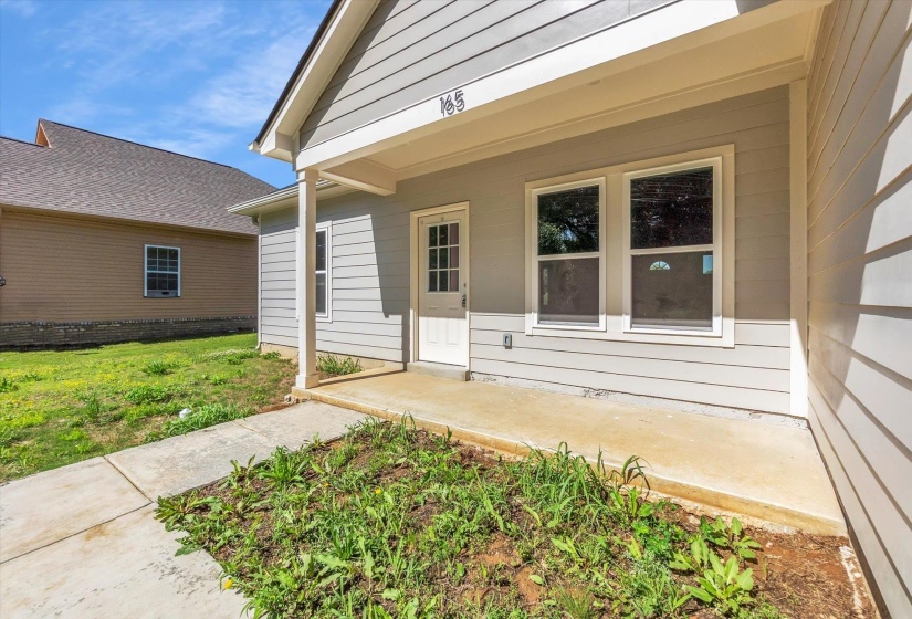 Light grey horizontal siding exterior with a covered porch featuring white support columns and a white paneled door with glass inserts
