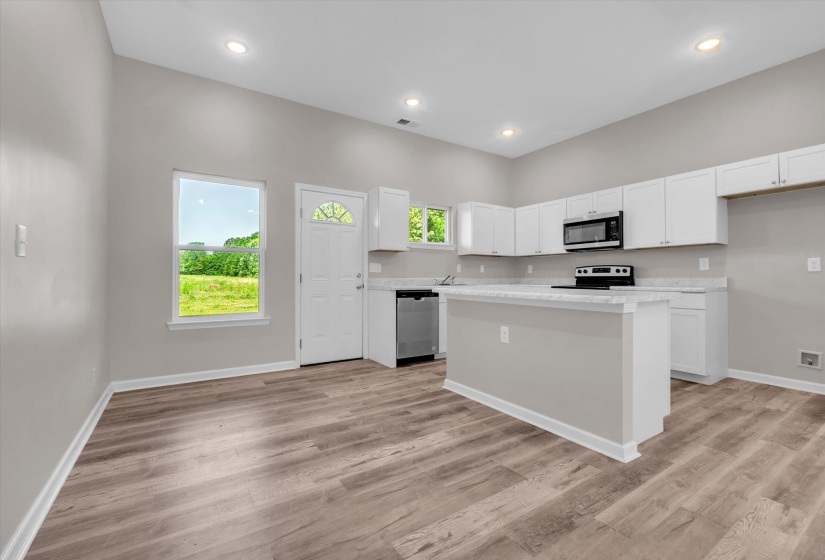 Open-concept kitchen featuring wood-finish flooring, white cabinetry, a central island with countertop, stainless steel appliances, and recessed lighting