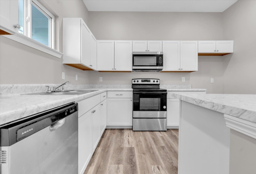 Modern kitchen featuring white cabinetry, light-toned countertops, stainless steel appliances, wood-finish flooring, and a large window