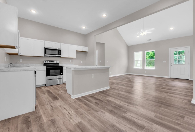 Open-concept kitchen and living area featuring wood-finish flooring, white cabinetry, and stainless steel appliances
