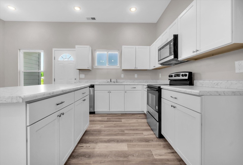 Spacious kitchen featuring white cabinetry, light-toned countertops, and wood-finish flooring