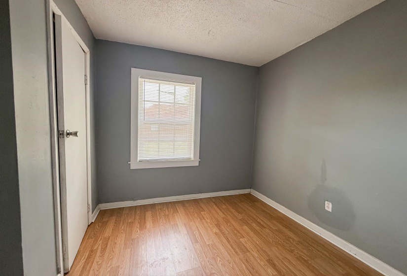 Room featuring wood-finish flooring, a single window with blinds, white trim, and a white interior door