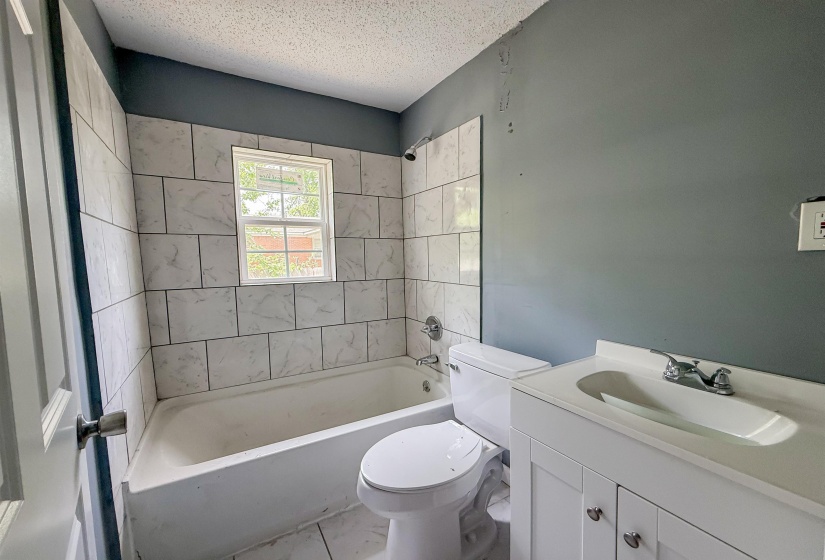 Bathroom featuring a tiled tub surround with a window, white vanity, integrated sink, and chrome fixtures