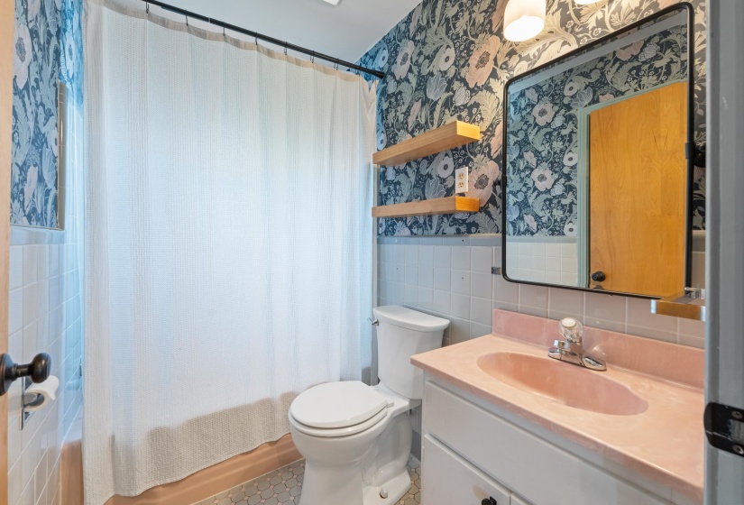 Bathroom with wallpapered walls, vanity, tile walls, and shower / bath combo.