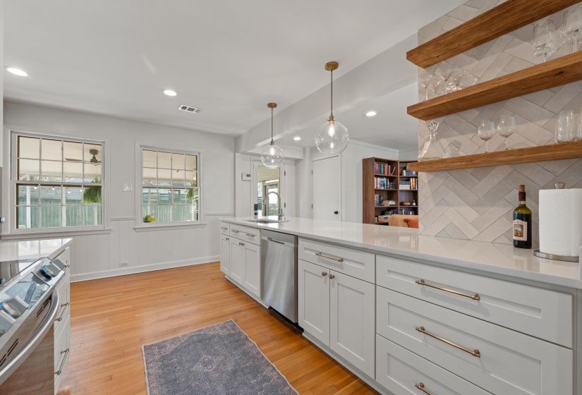 Kitchen featuring stainless steel appliances, hanging light fixtures, white cabinetry, light wood finished floors, and a wainscoted wall