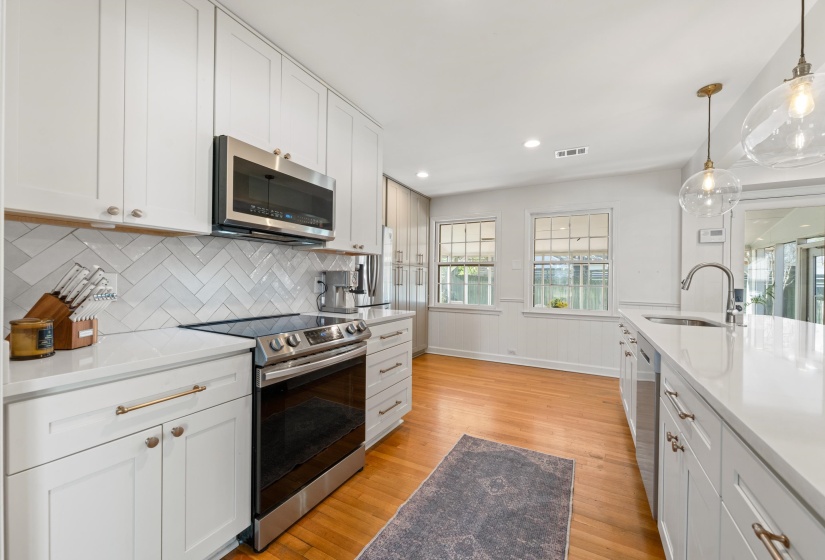 Kitchen with stainless steel appliances, white cabinets, light wood finished floors, light stone countertops, and hanging light fixtures