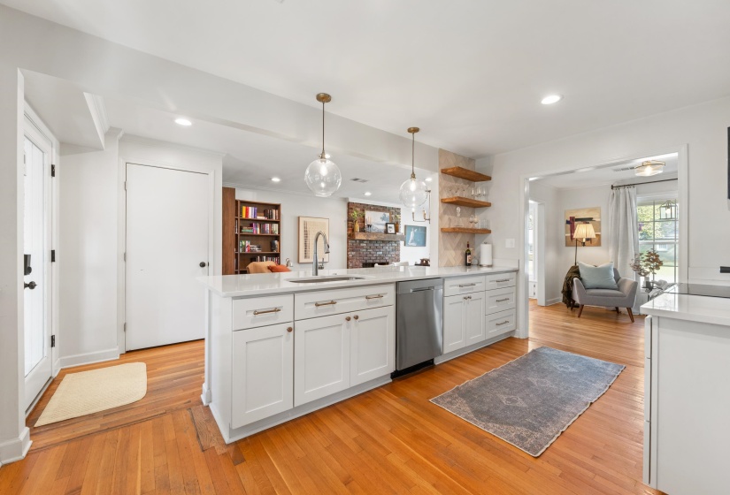 Kitchen featuring open floor plan, light wood-style flooring, pendant lighting, stainless steel dishwasher, and light stone counters