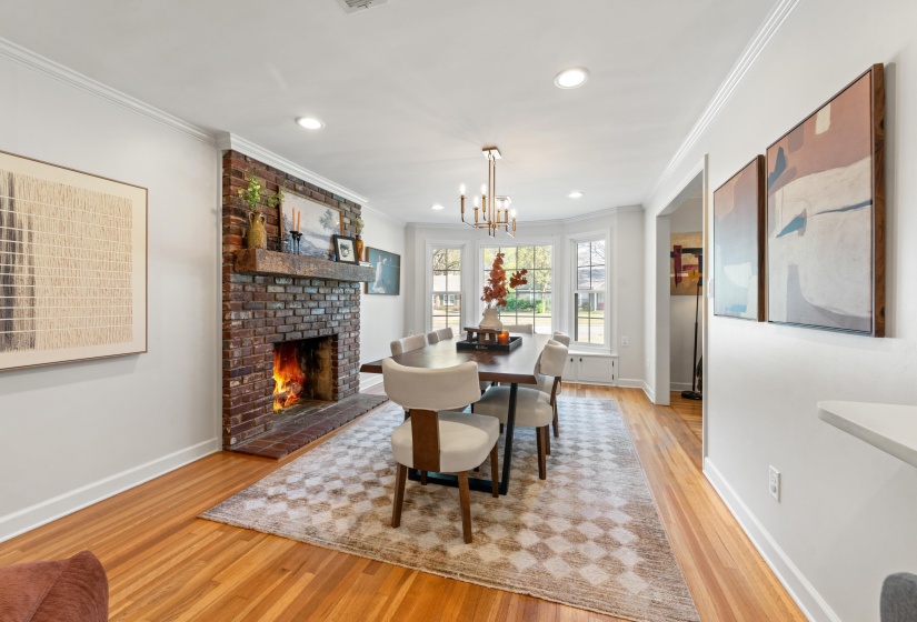 Dining area featuring light wood-type flooring, a brick fireplace, hanging lights, and ornamental molding