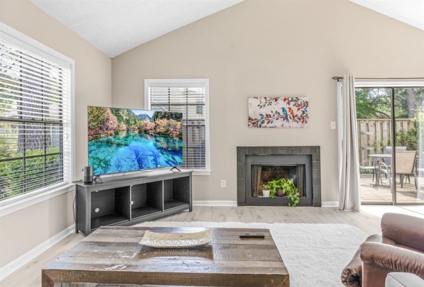 Living area featuring vaulted ceilings, wood-finish flooring, a dark-tiled fireplace, and sliding glass doors opening to an outdoor patio