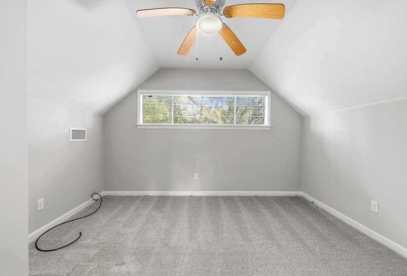 Vaulted ceiling room featuring light gray carpet flooring, a multi-pane window, and a ceiling fan with wood-finish blades