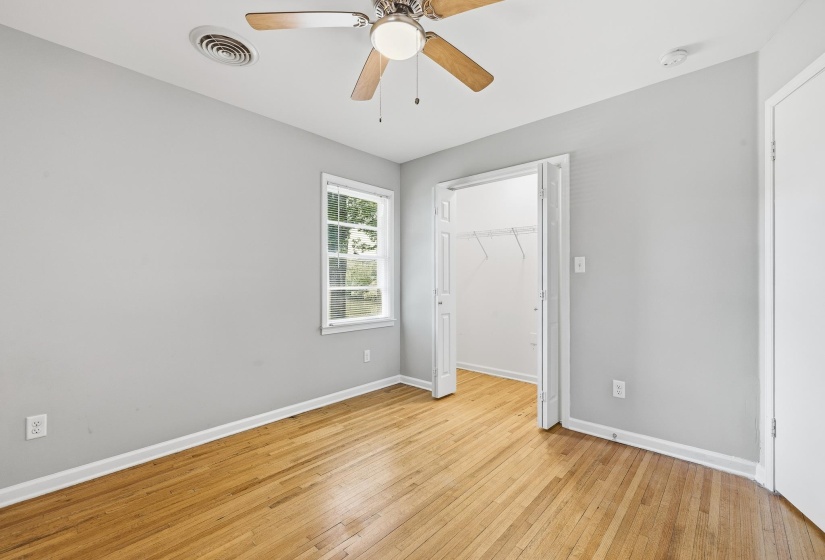 Room featuring wood-finish flooring, a ceiling fan with integrated lighting, and a window with white trim