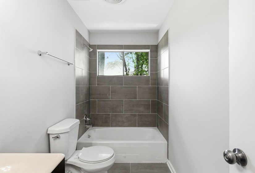 Full bathtub and shower combination featuring dark gray rectangular tile surround and a window