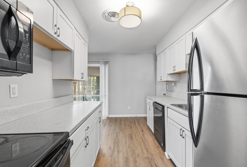 Galley-style kitchen featuring white cabinetry, light-toned countertops, and wood-finish flooring