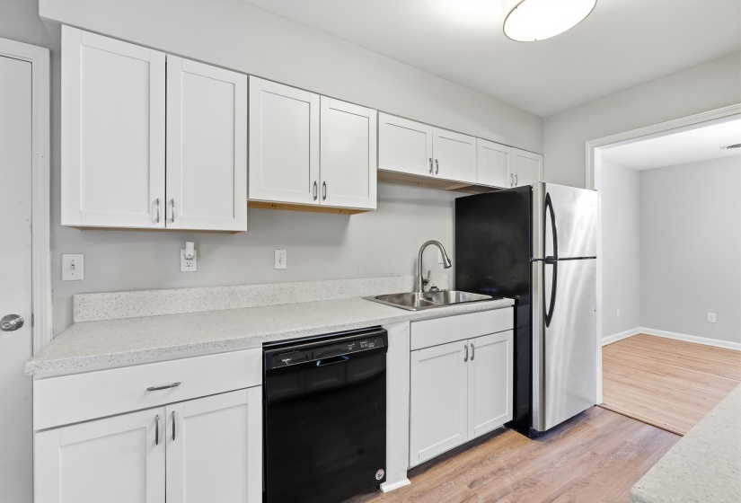Kitchen featuring white shaker-style cabinetry, light speckled countertops, a stainless steel refrigerator, and wood-finish flooring