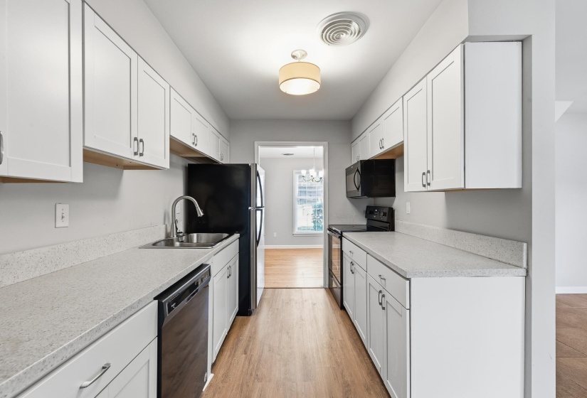 Galley kitchen featuring white cabinetry, light-toned countertops, wood-finish flooring, and black appliances