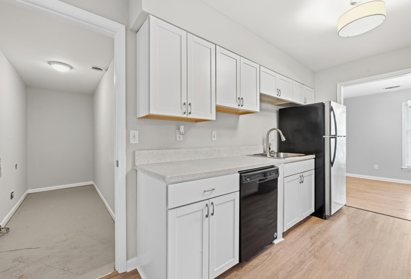 Kitchen featuring white cabinetry, light-toned countertops, a stainless steel sink with a gooseneck faucet, black appliances, and wood-finish flooring