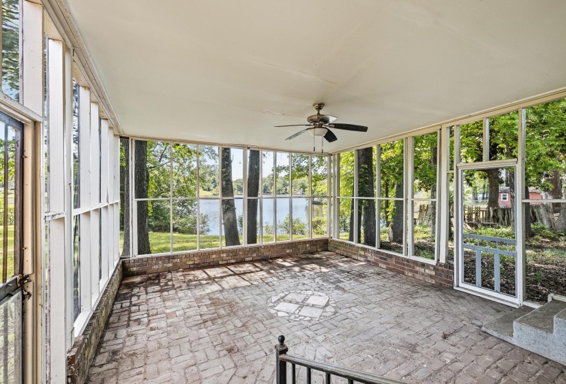 Screened porch featuring extensive glass panels, brick flooring, a ceiling fan, and a water backdrop